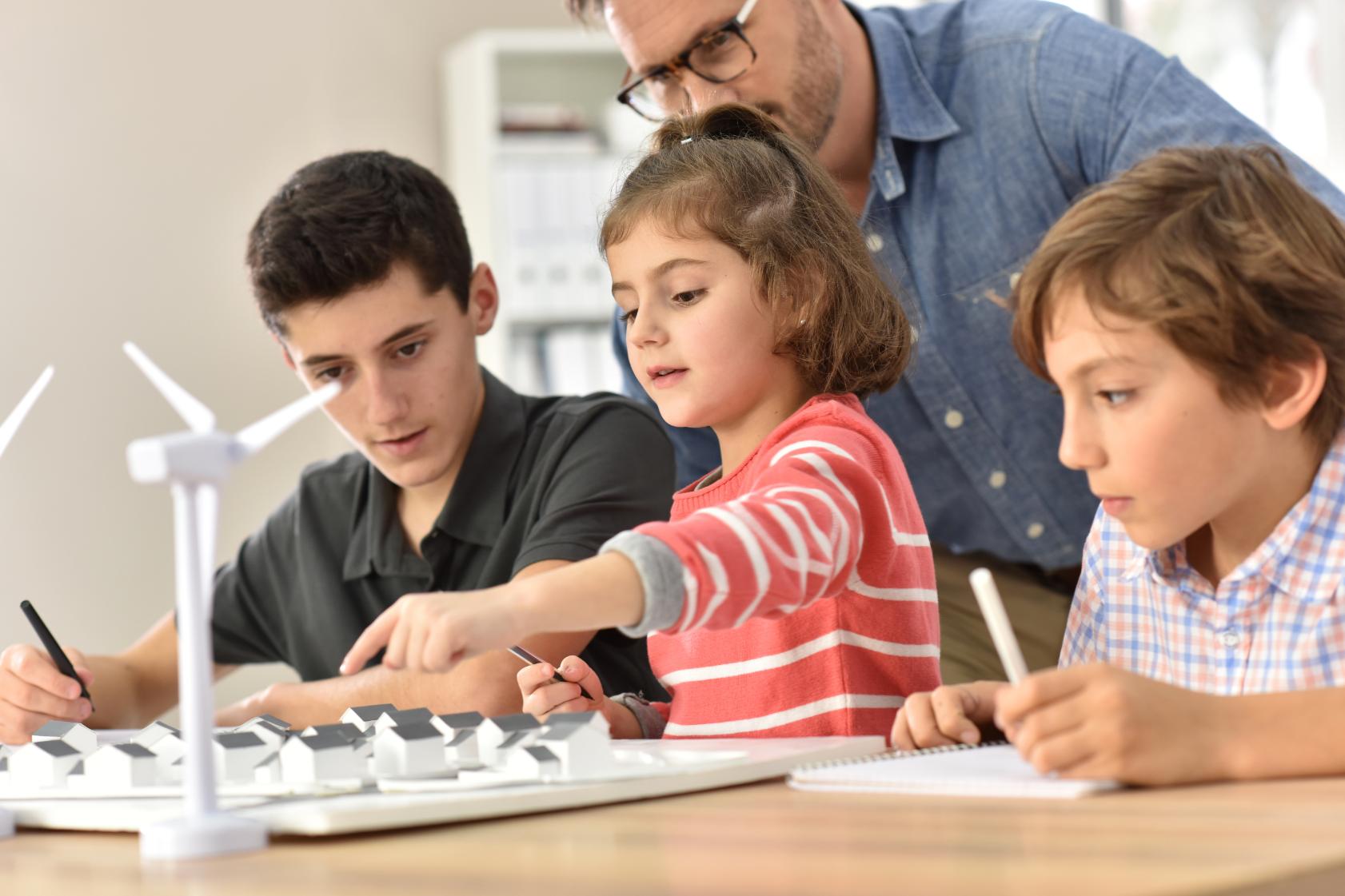 Three children and their father examining a model of a wind turbine
